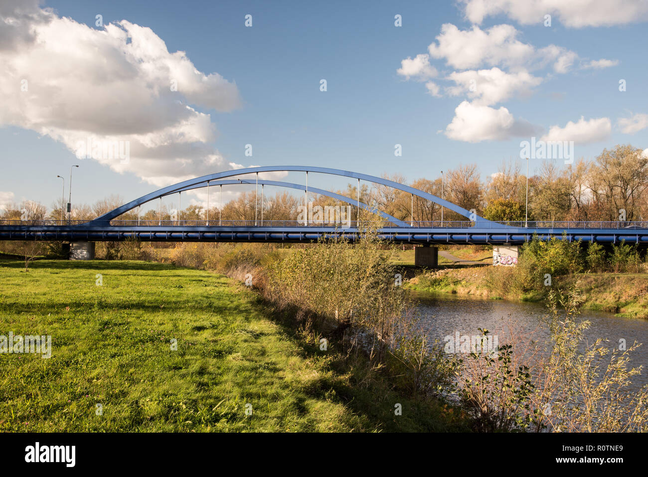 Blue road bridge con Olse river ed erba a Karvina città in Repubblica Ceca durante la bella giornata autunnale con cielo blu e poche nuvole Foto Stock