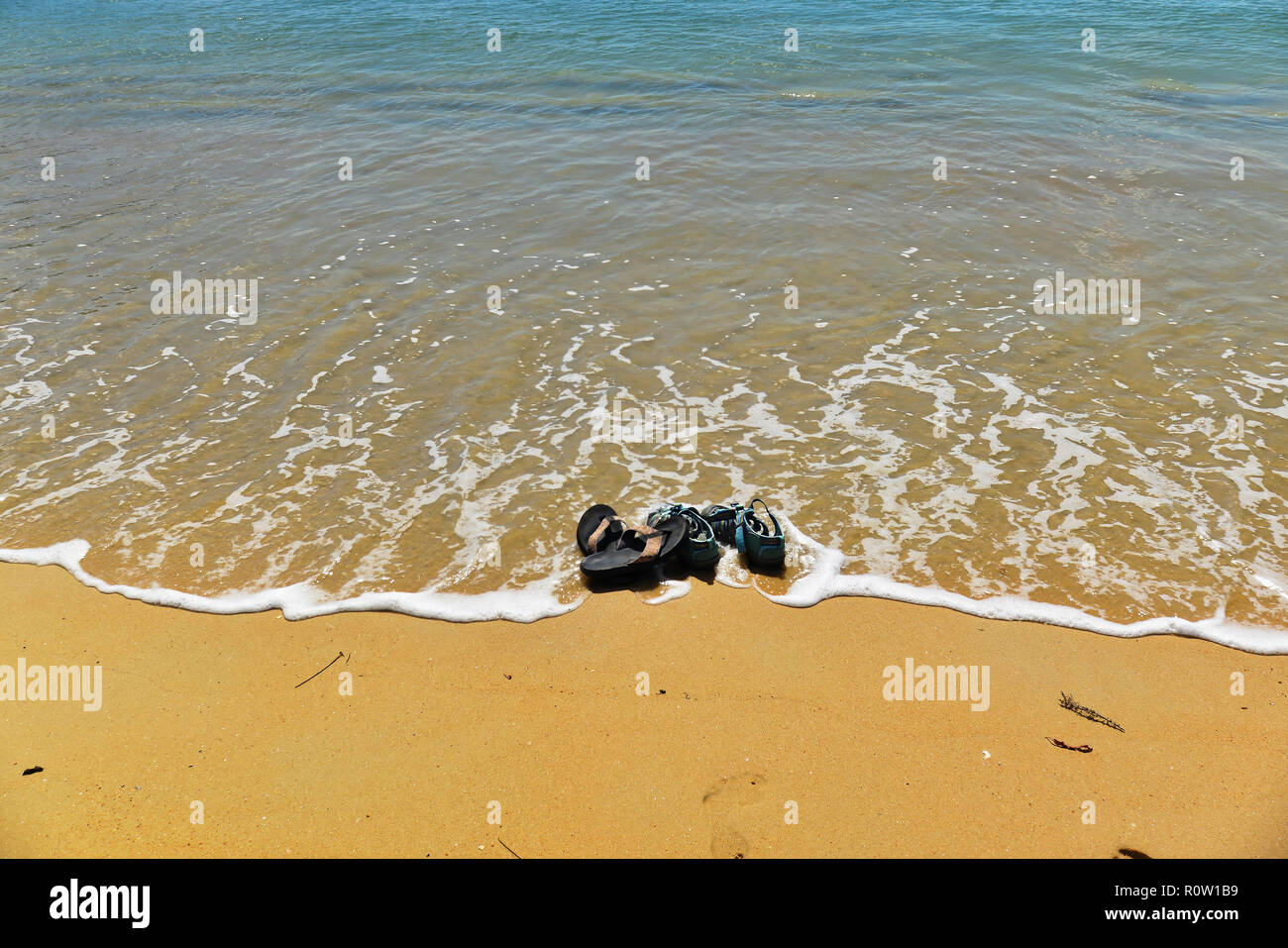 Il mare lambisce un paio di infradito e sandali a sinistra su una spiaggia dorata Foto Stock
