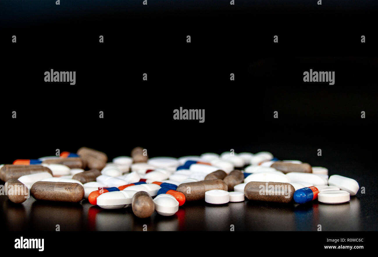 Pillole di diverse dimensioni, forme e colori con sfondo nero. Concetto di salute Foto Stock