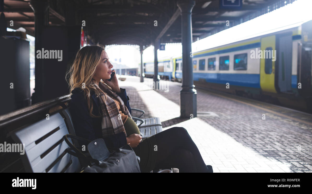 Donna incinta parlando al telefono mobile alla stazione ferroviaria Foto Stock