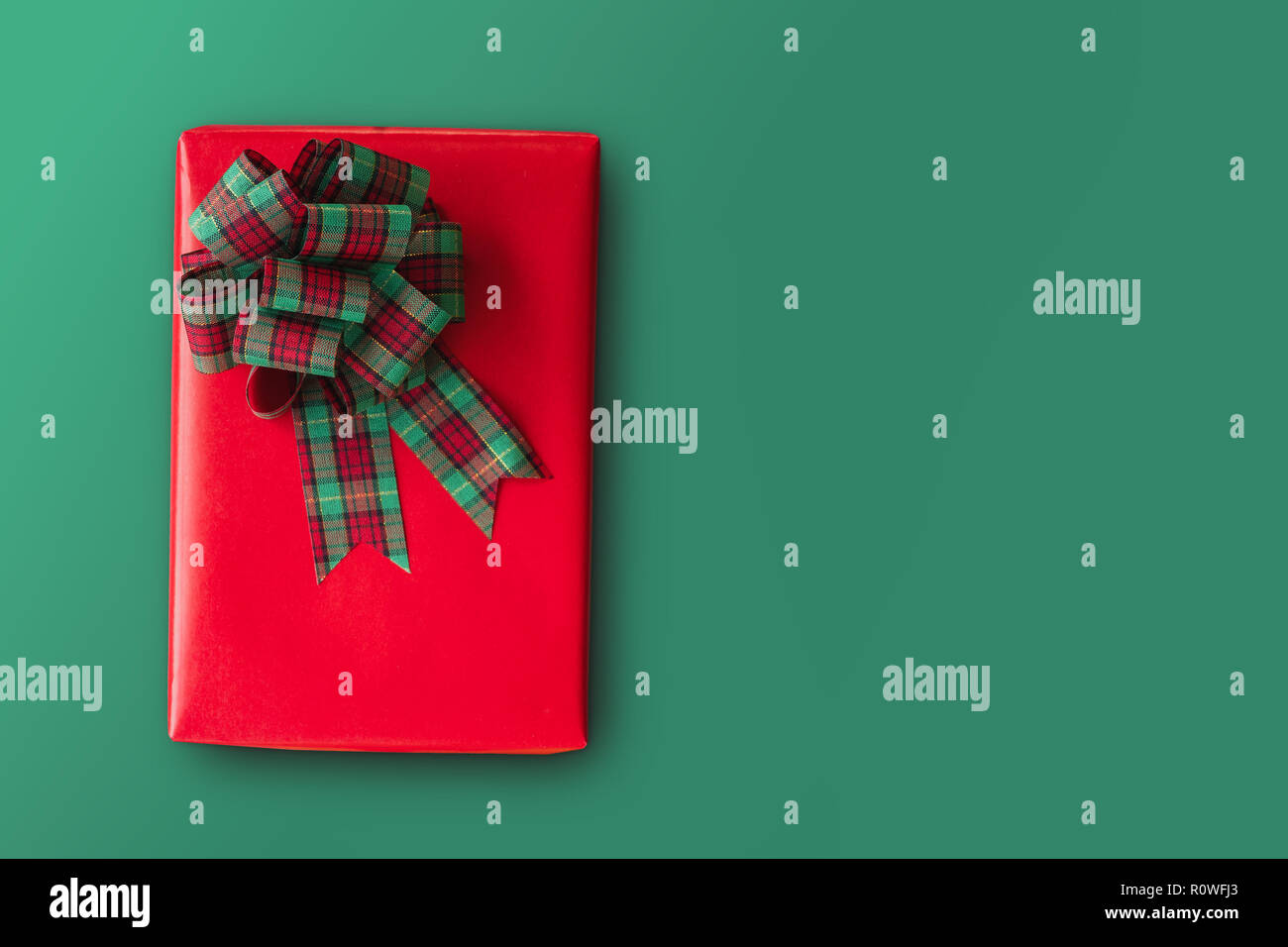 Red regalo di Natale scatola con nastro verde bow su sfondo verde con copia spazio e percorso di clipping su giftbox. Foto Stock
