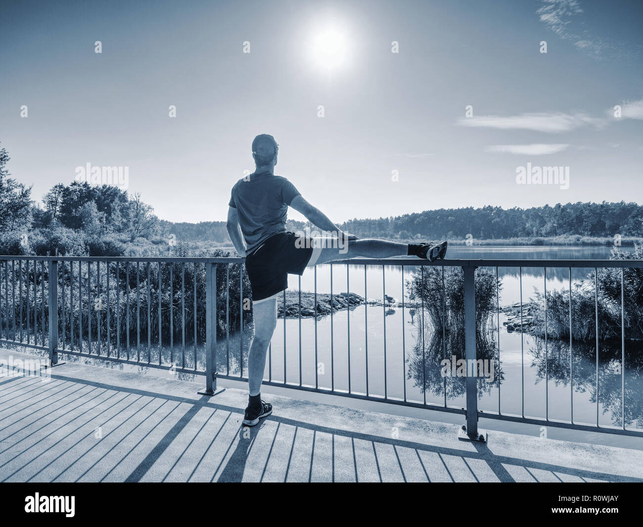 L uomo lo stiramento delle gambe prima di fare eseguire al di fuori all'interno di mattina di sole. Riscaldare i muscoli. Esercizio all'aperto sul lago di Ponte. Foto Stock