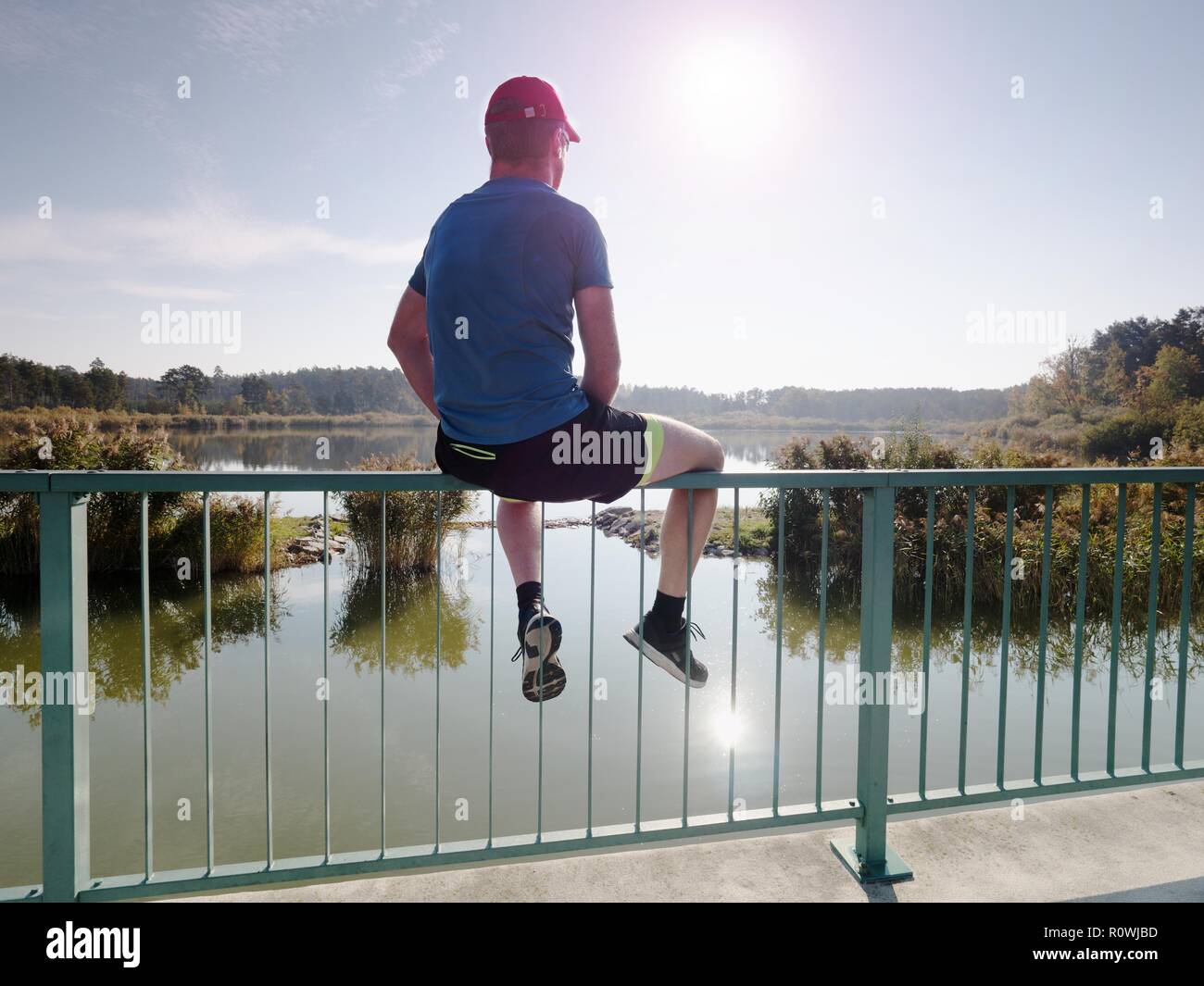 Unico Uomo in sport abbigliamento sedersi sul ponte il corrimano e guardare  oltre il lago di Sun Foto stock - Alamy