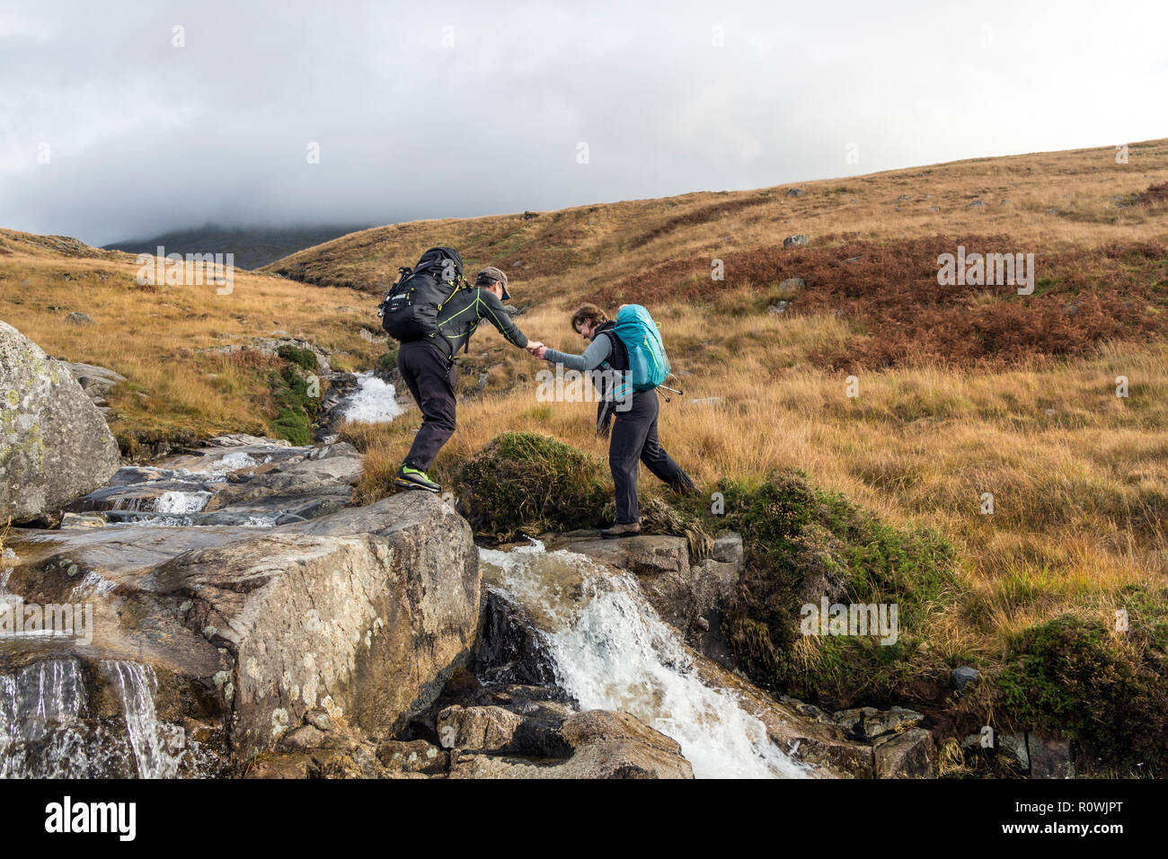 Walkers attraversando Hardrigg Gill durante la salita al monte di lieve lato, Lake District, Cumbria, Regno Unito Foto Stock