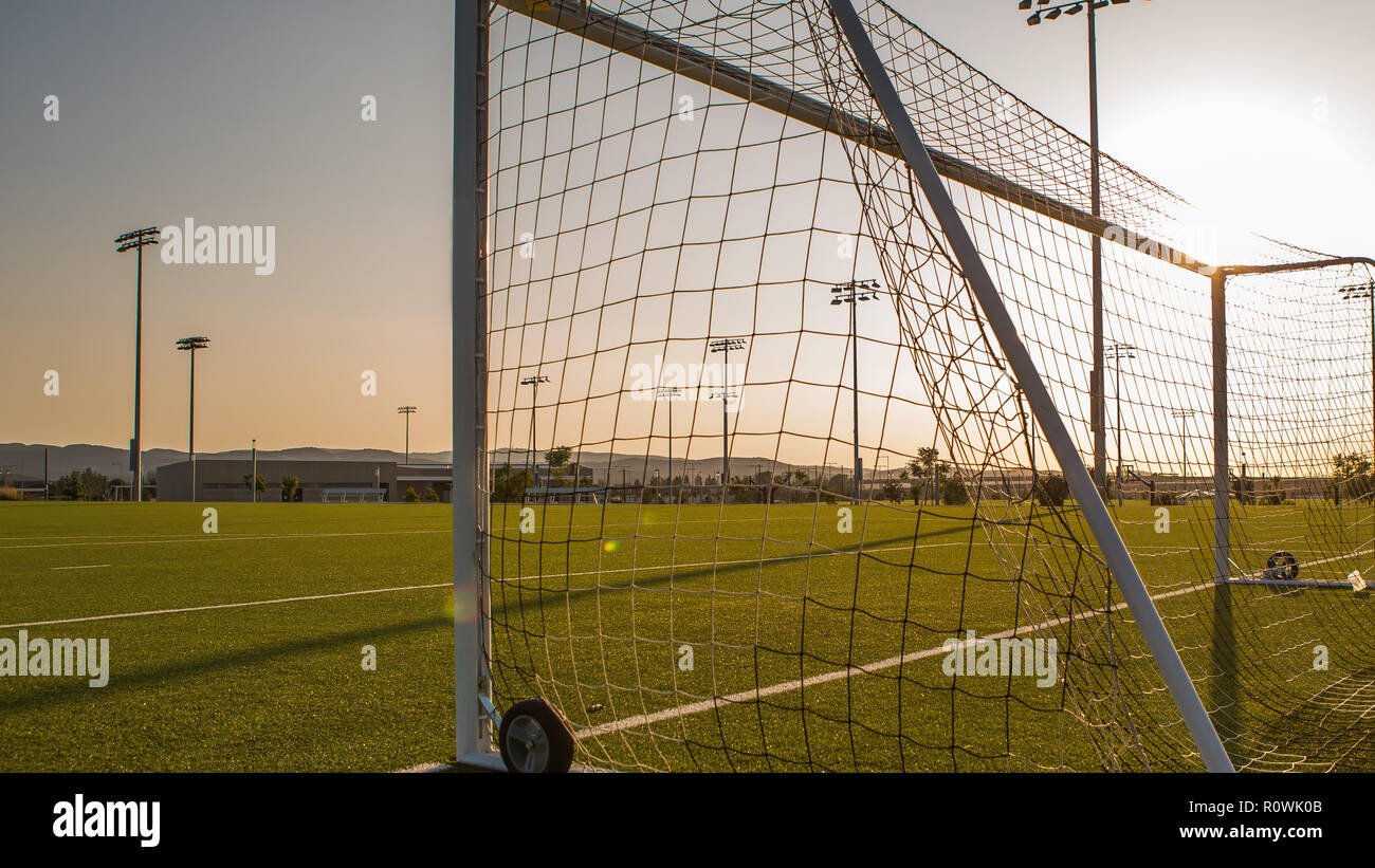 Svuotare il campo di calcio con Goalpost contro il tramonto, fari da stadio in vista Foto Stock