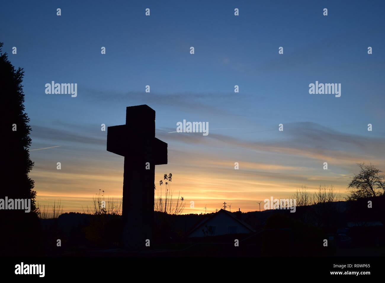 Sequenza temporale della sera Cielo di tramonto visto da dietro una sabbia croce di pietra scultura durante il sole al tramonto nel cimitero civile Reimsbach, Saarland, Foto Stock