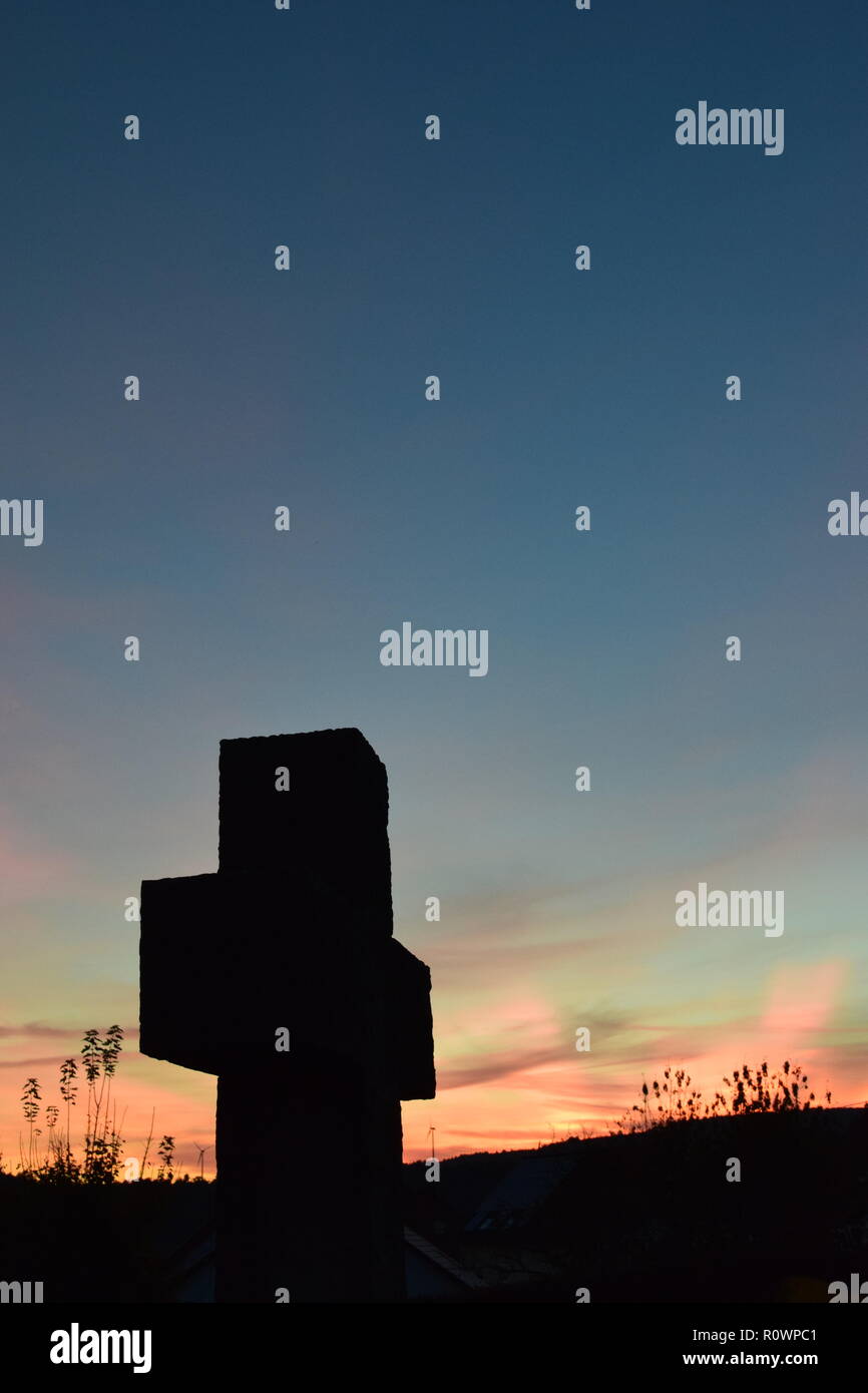 Sequenza temporale della sera Cielo di tramonto visto da dietro una sabbia croce di pietra scultura durante il sole al tramonto nel cimitero civile Reimsbach, Saarland, Foto Stock