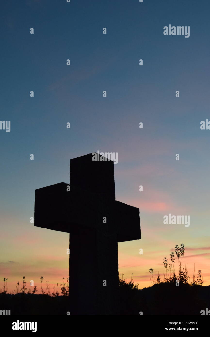 Sequenza temporale della sera Cielo di tramonto visto da dietro una sabbia croce di pietra scultura durante il sole al tramonto nel cimitero civile Reimsbach, Saarland, Foto Stock