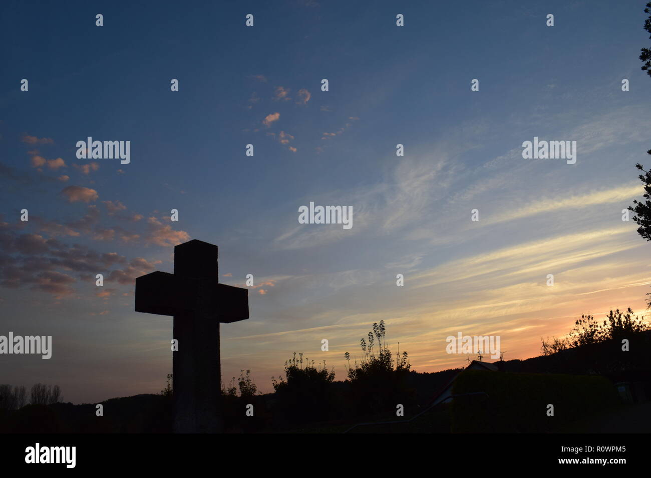 Sequenza temporale della sera Cielo di tramonto visto da dietro una sabbia croce di pietra scultura durante il sole al tramonto nel cimitero civile Reimsbach, Saarland, Foto Stock