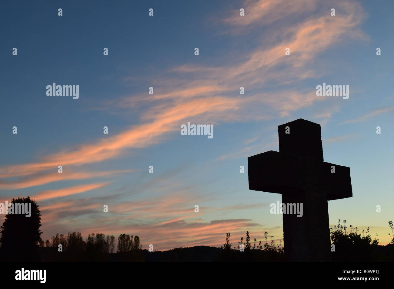 Sequenza temporale della sera Cielo di tramonto visto da dietro una sabbia croce di pietra scultura durante il sole al tramonto nel cimitero civile Reimsbach, Saarland, Foto Stock