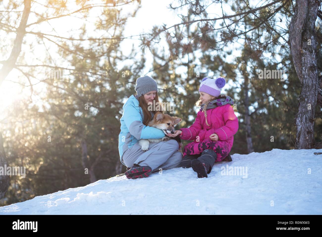 La famiglia felice - sorridente madre e figlia con poco carino corgi fluffy cucciolo al giorno d'inverno Foto Stock