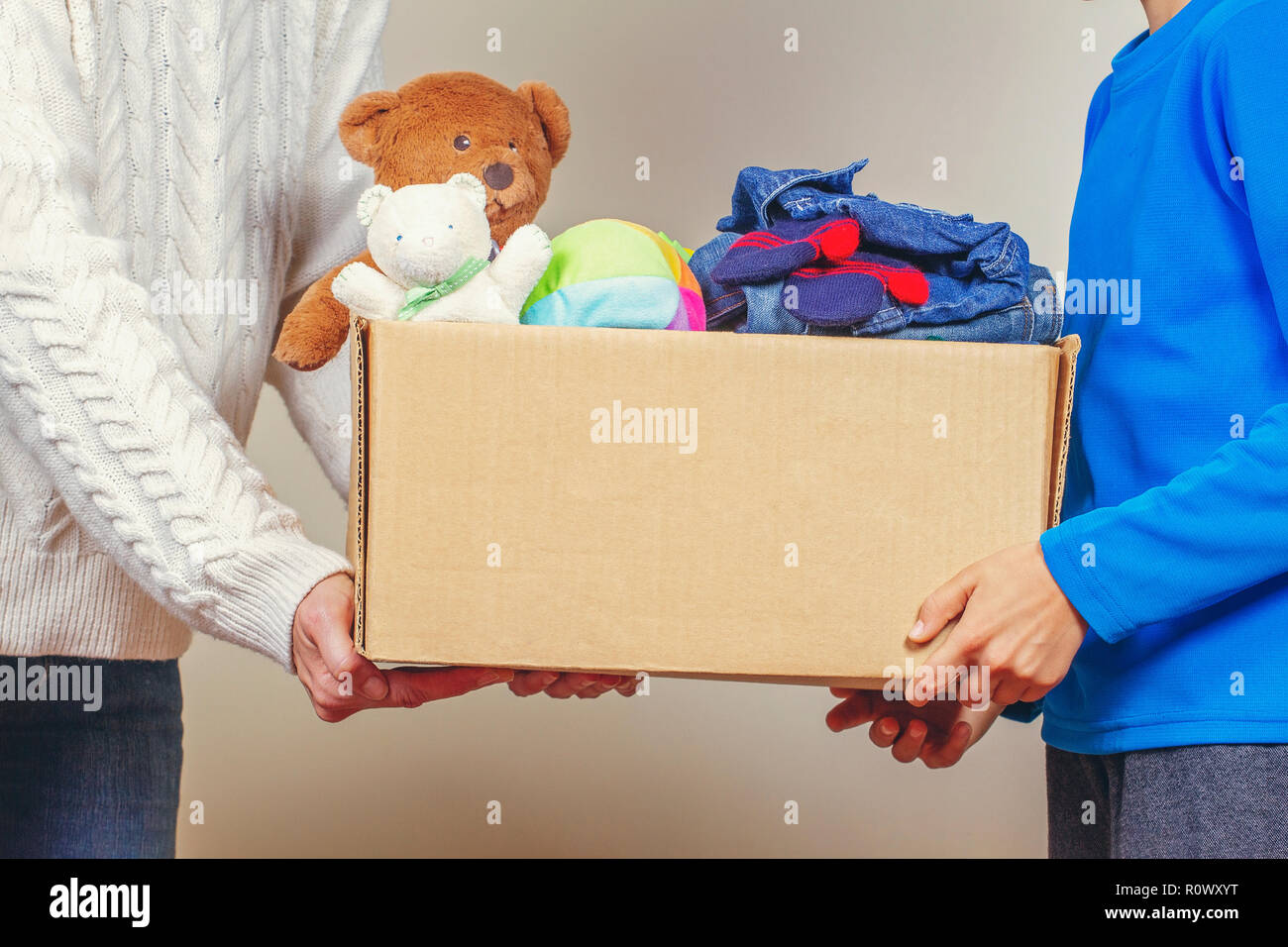 Concetto di donazione. Donare il box con abiti, libri e giocattoli nei membri della famiglia mano Foto Stock