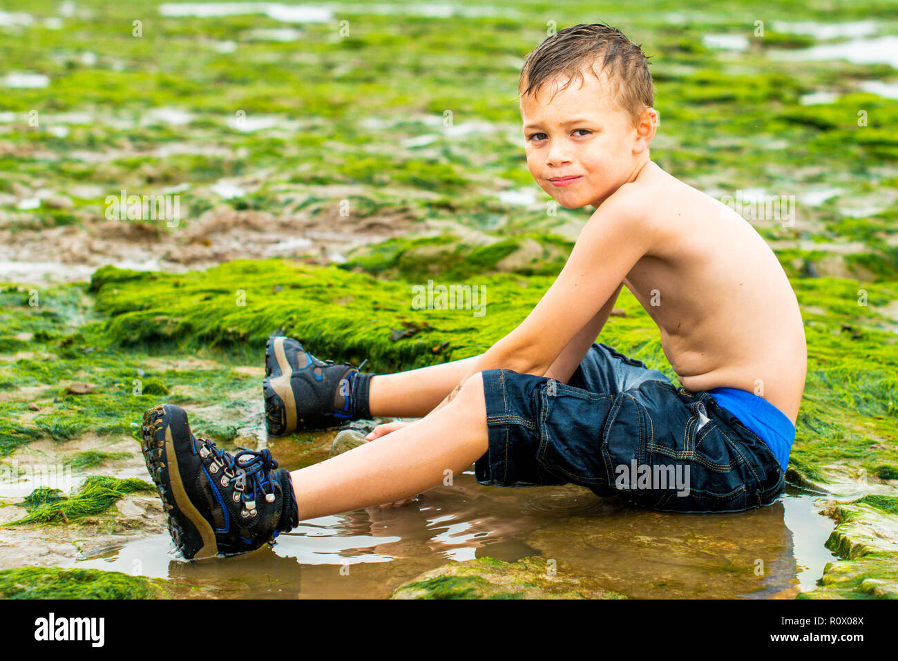 Bello active ragazzino con ADHD, autismo, sindrome di Aspergers giocando nel freddo alghe, alghe e acqua di mare su Walton sul Naze beach, Essex Foto Stock