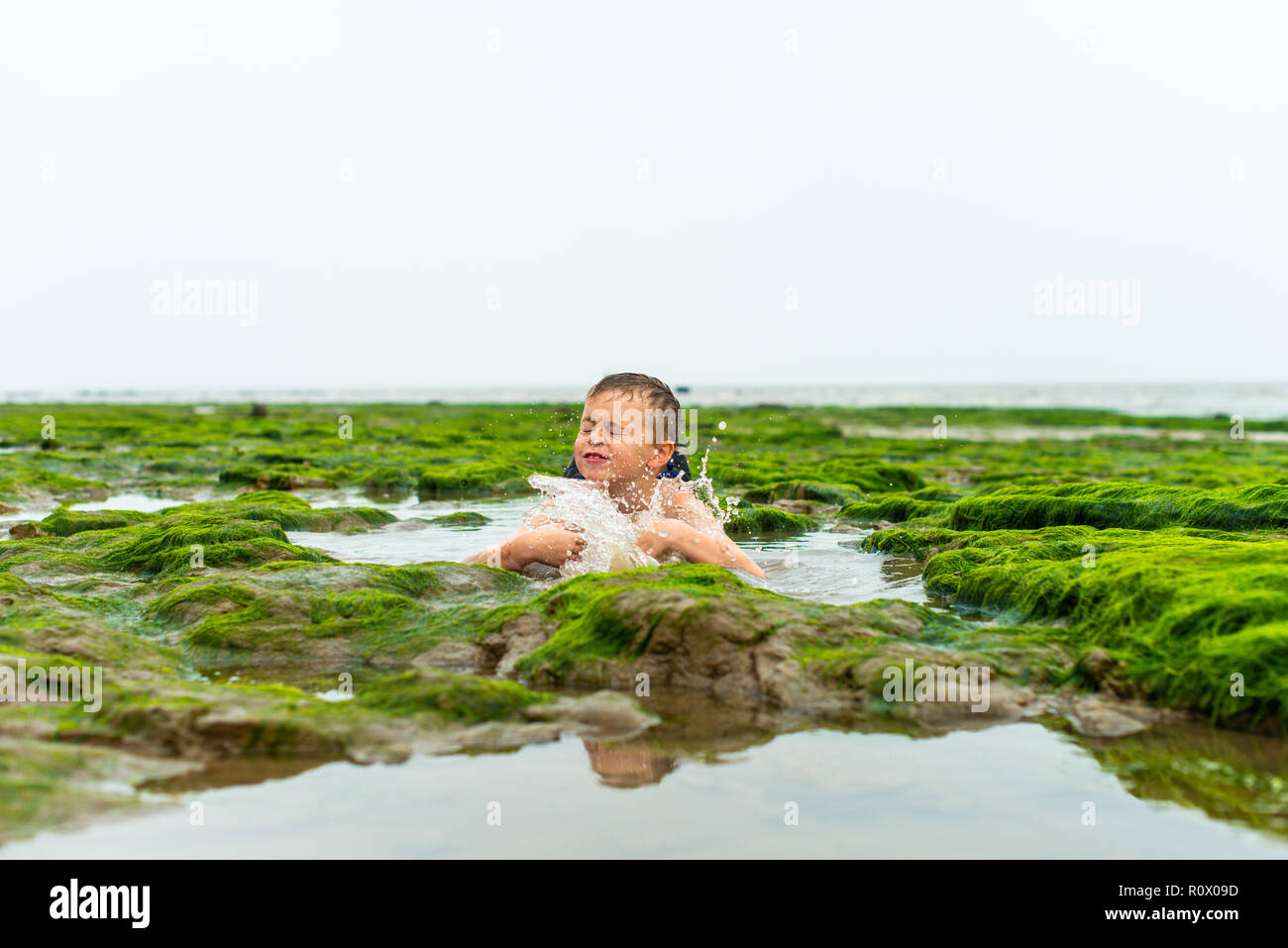 Bello active ragazzino con ADHD, autismo, sindrome di Aspergers giocando nel freddo alghe, alghe e acqua di mare su Walton sul Naze beach, Essex Foto Stock