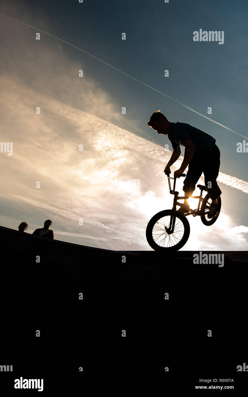 Un rider BMX presso il Plaza, Central Forest park a Stoke on Trent in sella alta e fare acrobazie in silhouette come il sole tramonta Foto Stock