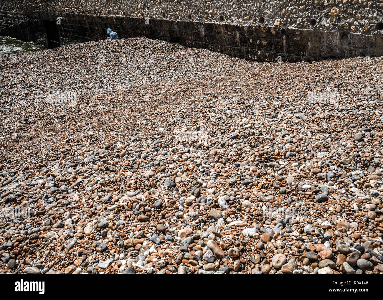 Solitaria figura incappucciato su brighton spiaggia ghiaiosa Foto Stock