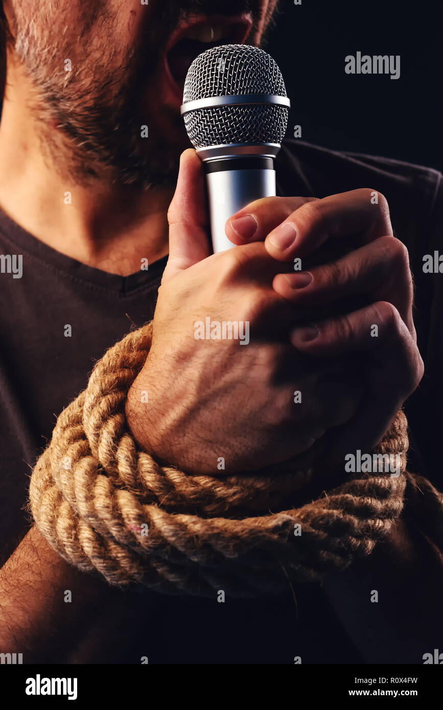La libertà di parola, immagine concettuale con maschio persona in possesso di un microfono con le mani legate in corde, bassa immagine chiave Foto Stock