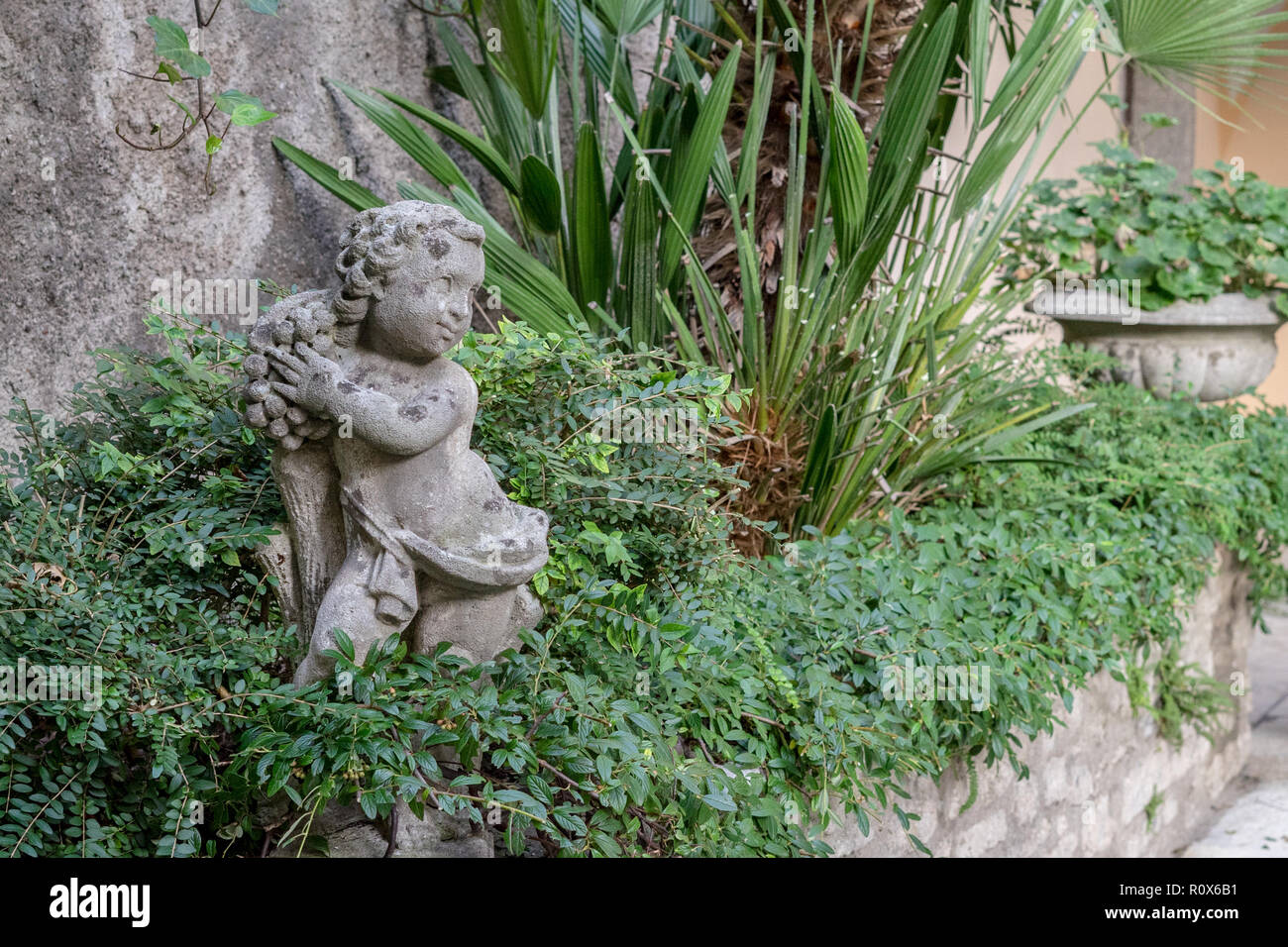 Parete in giardino con piante verdi e una piccola scultura Foto Stock