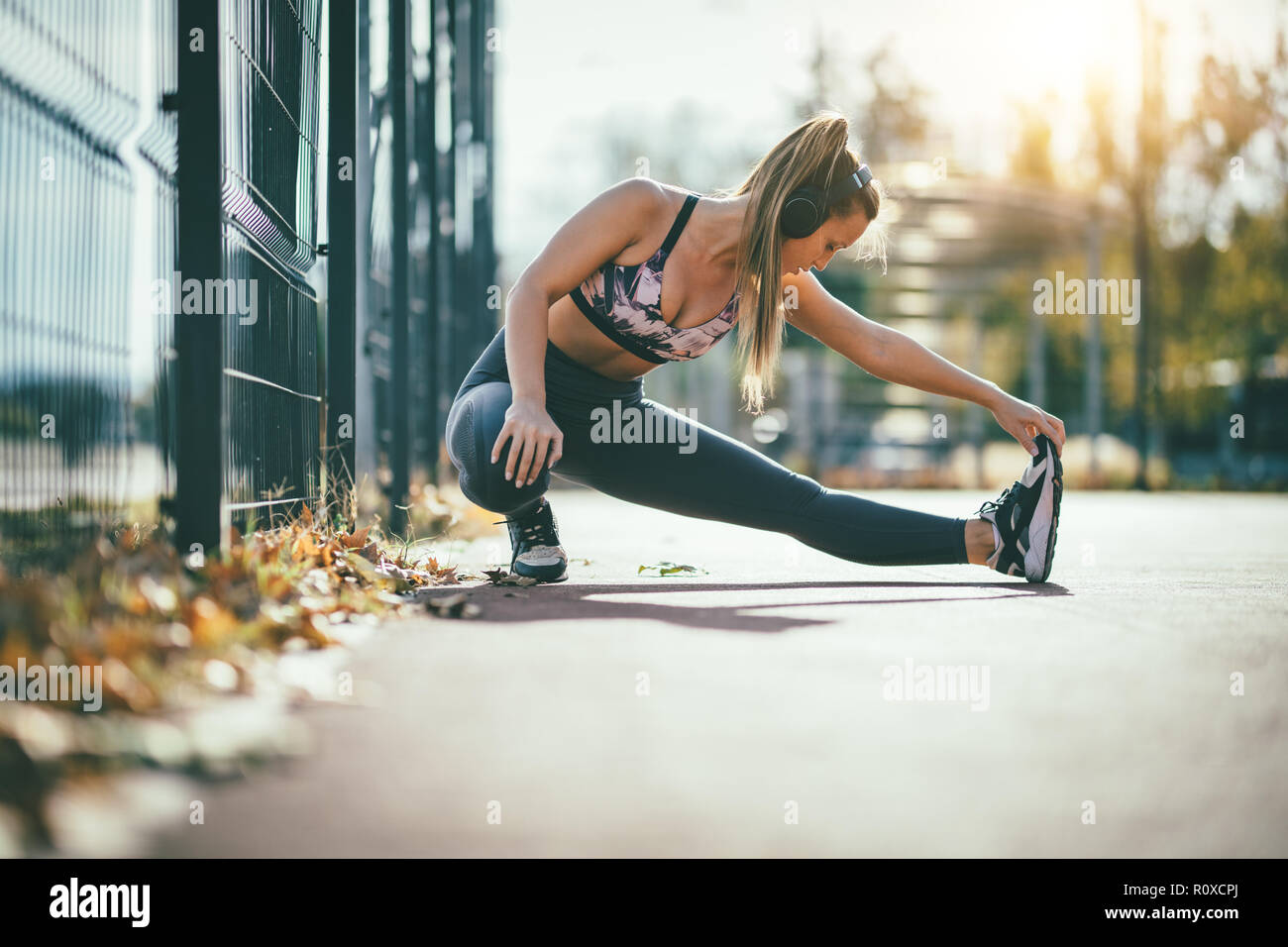 Giovani femmine runner con le cuffie sulle orecchie di lei, facendo stretching esercitare sulla recinzione metallica, preparazione per allenamento mattutino. Foto Stock