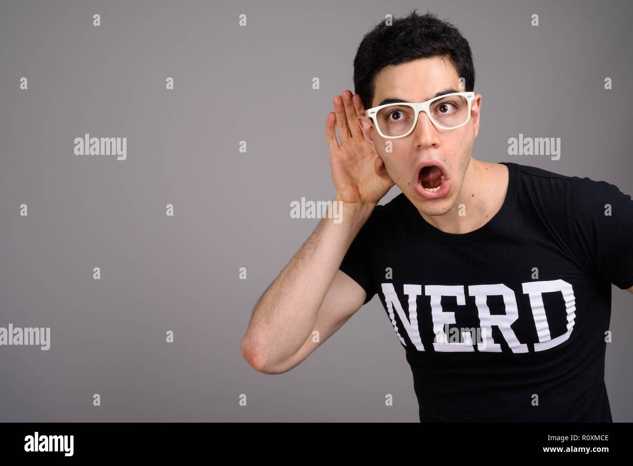Giovane bello nerd Uomo con occhiali contro uno sfondo grigio Foto Stock