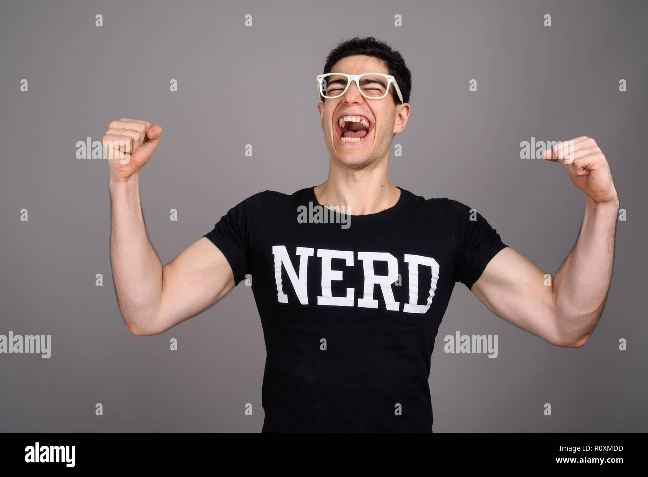 Giovane bello nerd Uomo con occhiali contro uno sfondo grigio Foto Stock