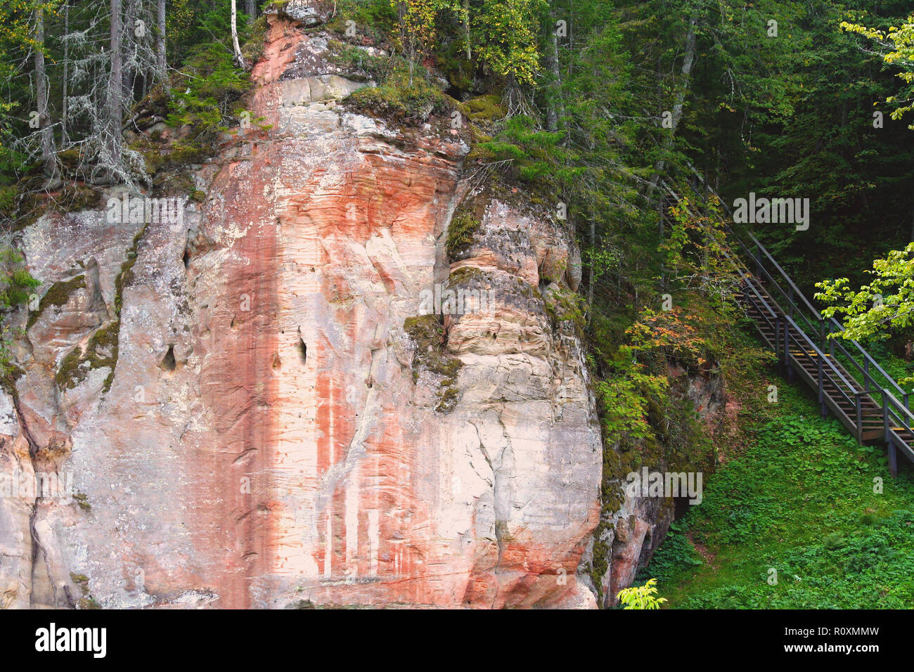 Un grosso pezzo di roccia con striature di colore rosso e bianco, accanto ad esso è un ponte che conduce verso l'alto e asciutto e verdi alberi crescono intorno, leggermente ingiallimento Foto Stock