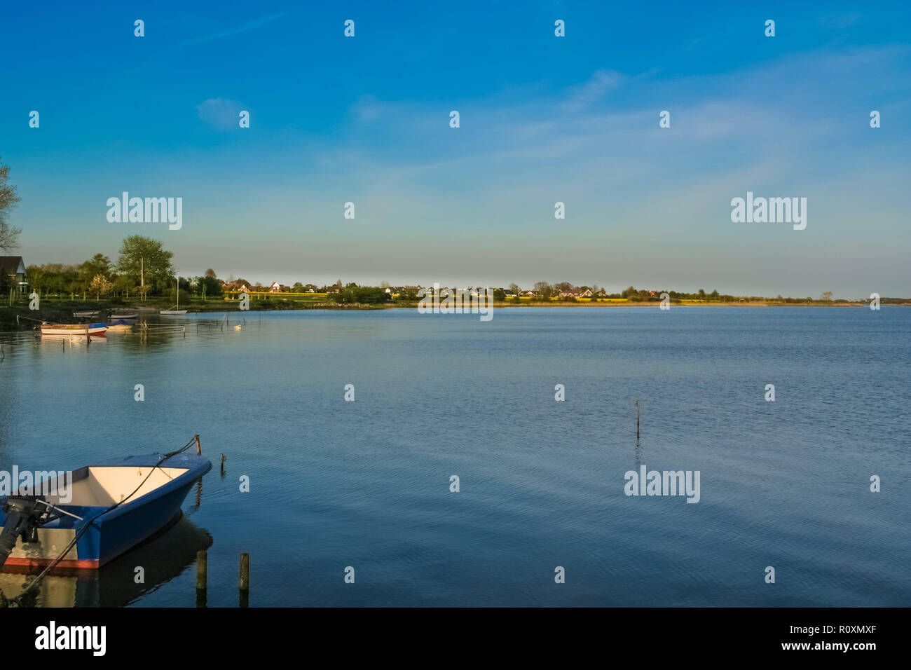 Vista panoramica di un legato motoscafo in acqua tranquilla e un villaggio lontano su un bellissimo tramonto giornata con un cielo blu a Fehmarn island in Germania. Foto Stock