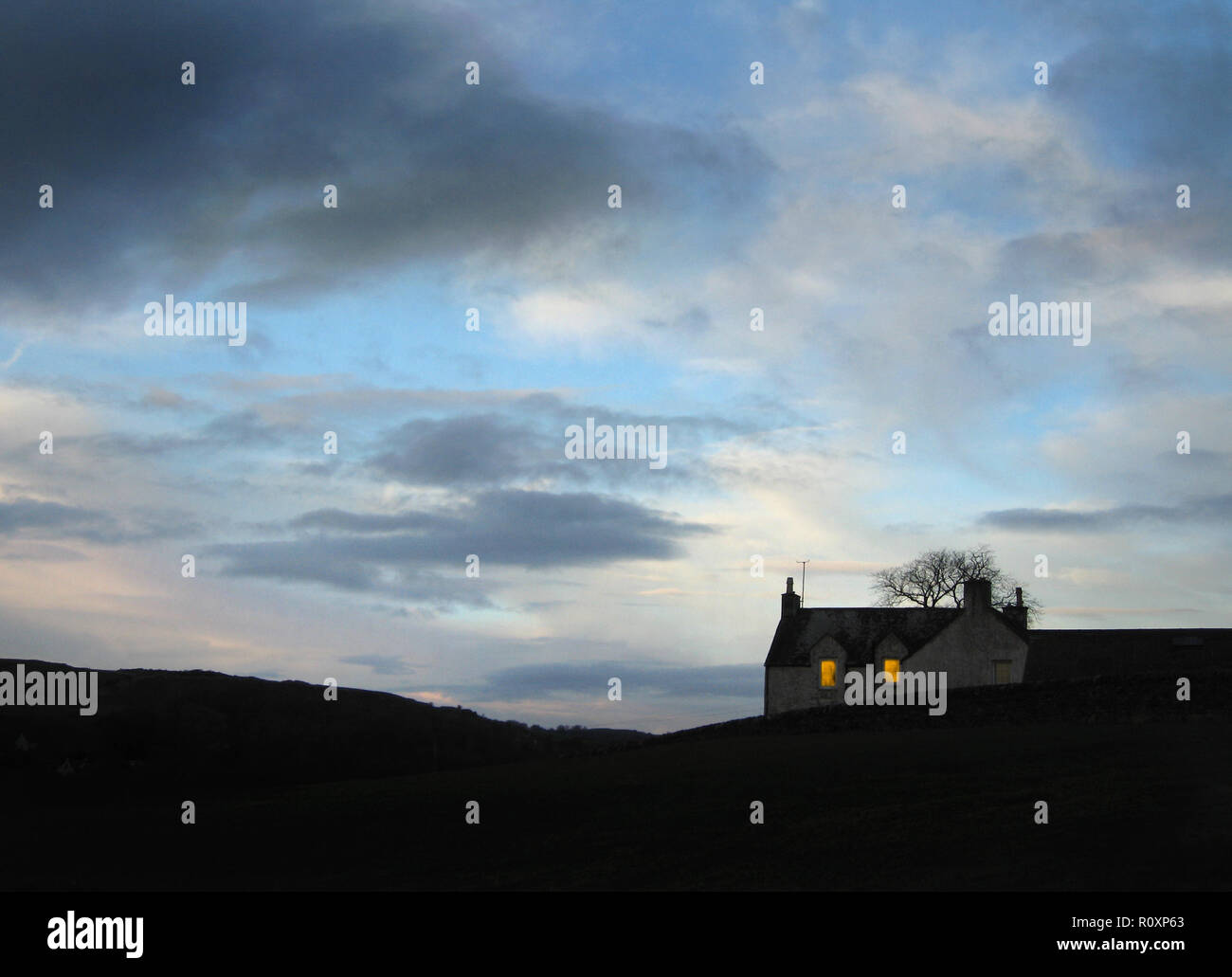 Una casa solitaria su una collina desolata in Scozia. Gli occupanti sono a casa e brillano una luce nel buio dalle finestre - come il cielo si oscura Foto Stock
