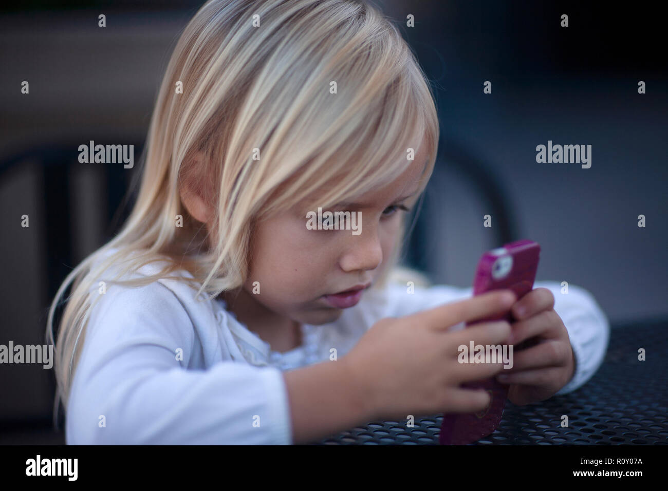 Giovane ragazza bionda guardando rosa telefono cellulare con un intenso sguardo sul suo viso. Foto Stock