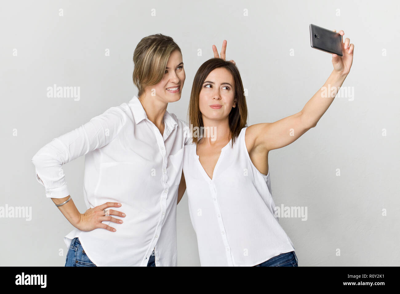 Due giovane donna in maglia bianca per divertirsi facendo selfie. Studio shot contro uno sfondo bianco Foto Stock