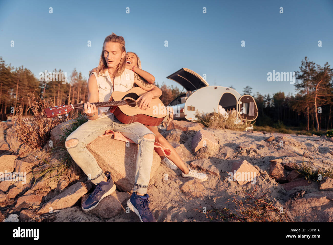 Uomo con lunghi capelli biondi indossa abbigliamento denim a suonare la chitarra Foto Stock