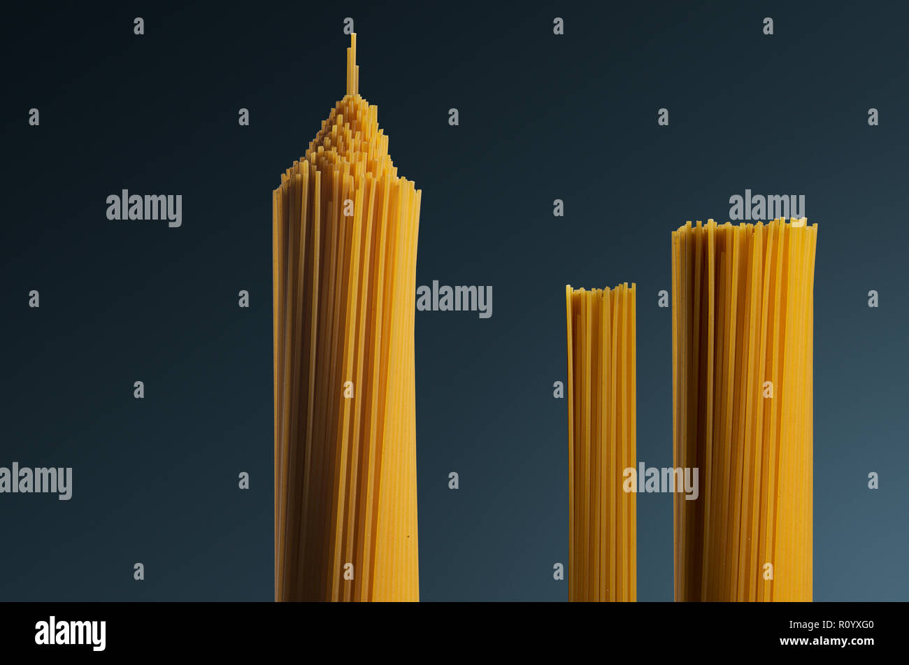 Tre grappoli di materie non cotte a forma di spaghetti come strutture a torre contro uno sfondo grigio Foto Stock
