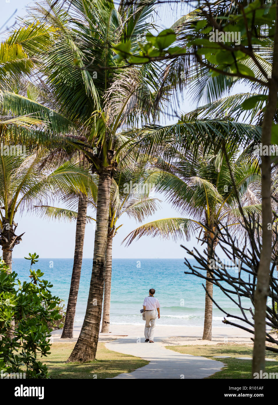 Un uomo a piedi giù per un sentiero verso la spiaggia tropicale in Sanya Hainan Island in Cina. Foto Stock