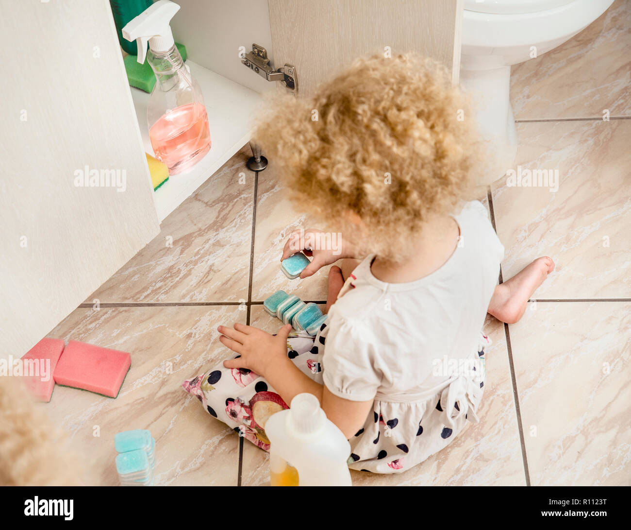 Incustoditi bambine giocare tranquillamente da bagno con pericolose sostanze chimiche di uso domestico. Pericolo per la sicurezza in casa del concetto. Tenere lontano dalla portata dei bambini di raggiungere. Foto Stock