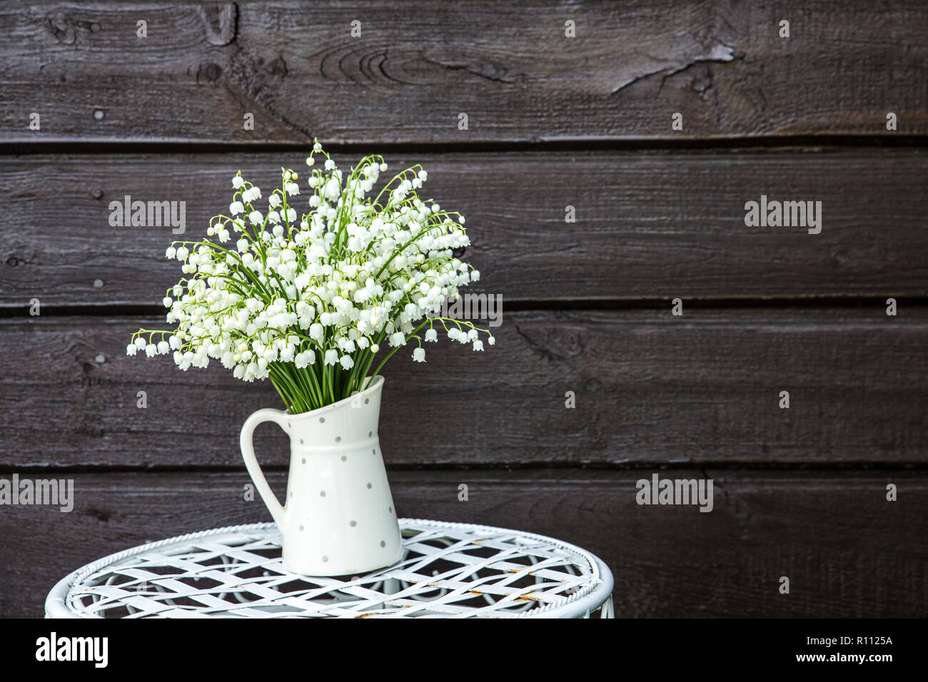 Bouquet di bianco fiori recisi il giglio della valle (convallaria majalis) in un secchio di zinco forma di vaso, all'aperto su un bianco fiore fantasia stand, marrone wo Foto Stock