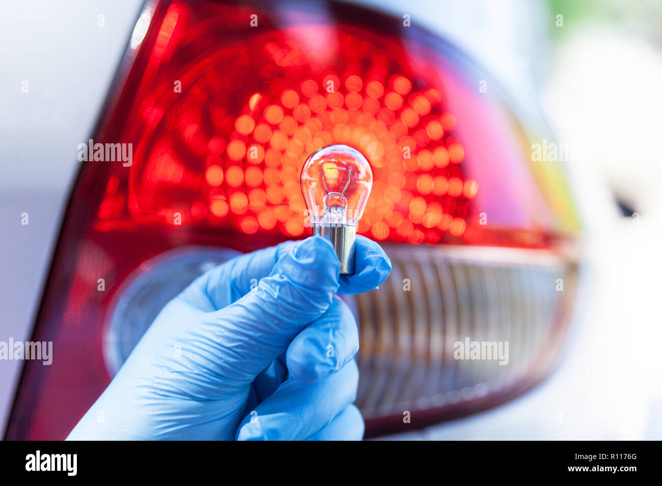 Una mano in blu guanto tenendo un auto, Lampadina luce di coda in background Foto Stock