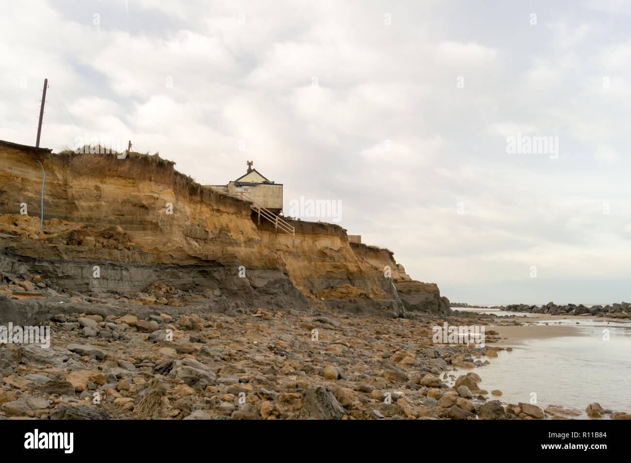 Casa sul bordo della scogliera lavata via dal mare, erosione costiera, il riscaldamento globale, l'aumento del livello del mare, Happisburgh Norfolk, Regno Unito. veduta distante. Foto Stock