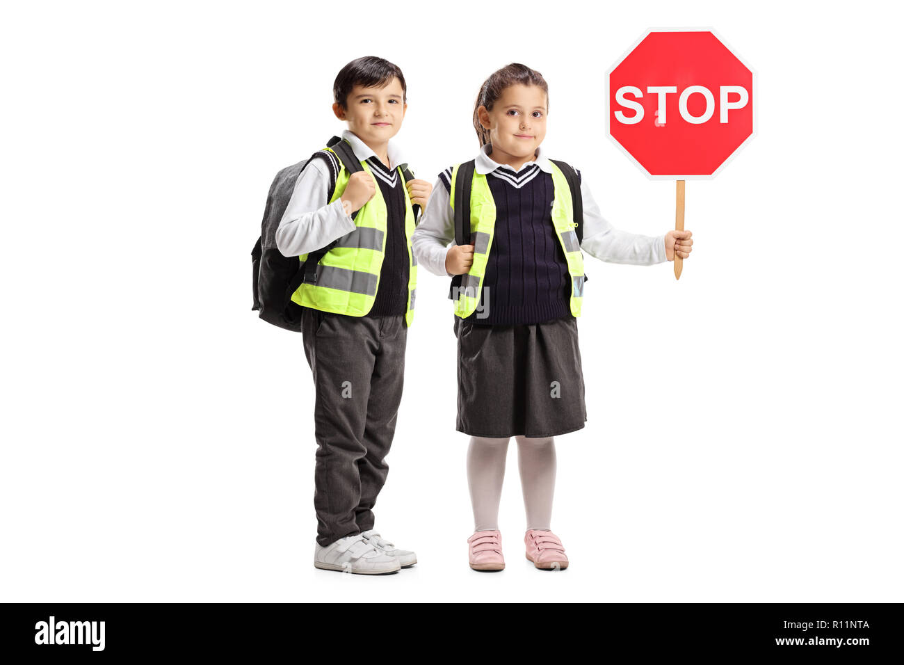 A piena lunghezza ritratto di uno scolaro e una scolaretta con giubbotti di sicurezza e di un segnale di stop isolato su sfondo bianco Foto Stock