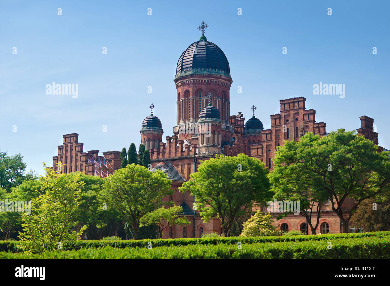 La facciata della capmus principale di Yuriy Fedkovych Chernivtsi Università Nazionale contro lo sfondo del giardino con alberi verdi e un elevato lante Foto Stock