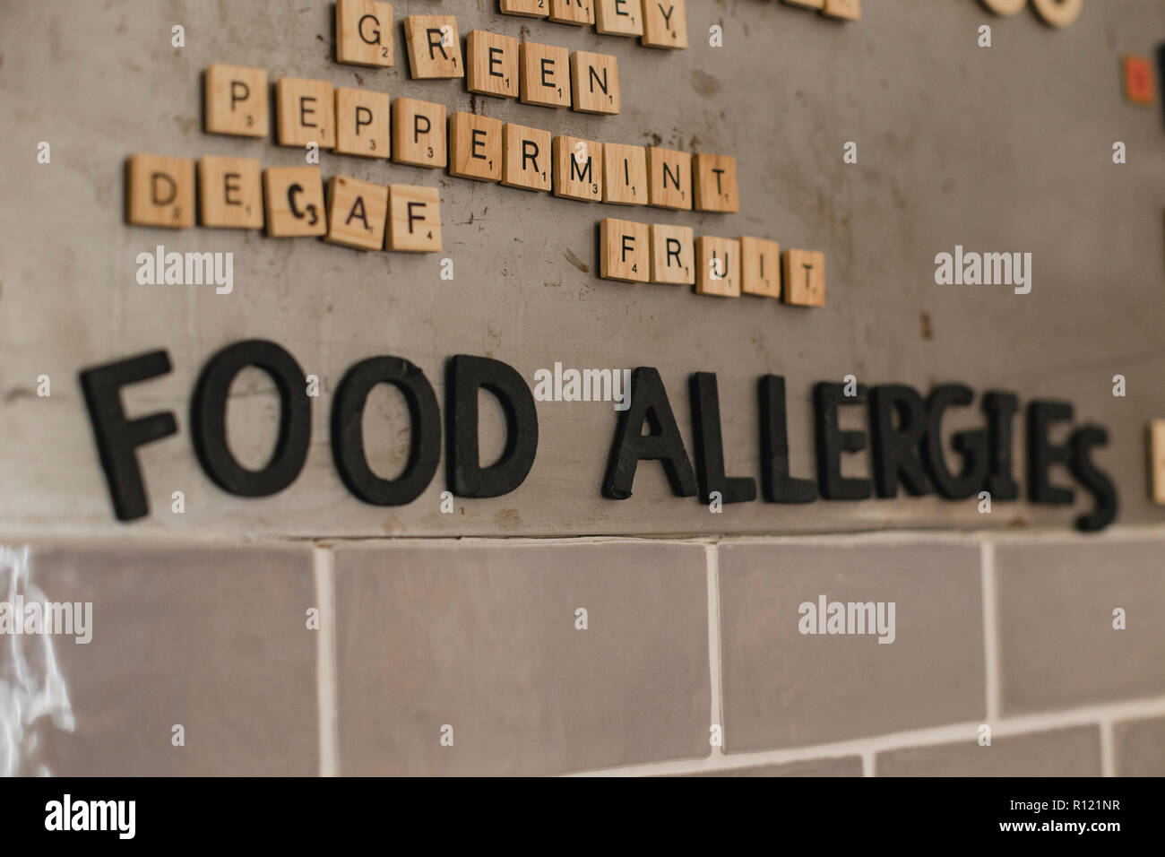 Basso angolo di visione delle allergie alimentari menu sulla parete in una caffetteria. Essi hanno utilizzato poco piastrella lettere per mostrare le parole. Foto Stock