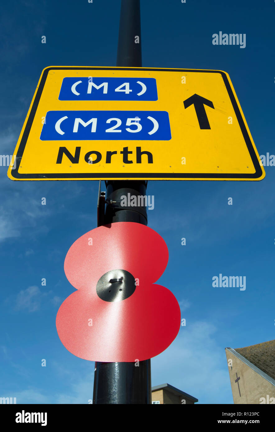 Oversized ricordo il papavero attaccato ad un lampione sotto un cartello stradale per la m4 e la m25 in direzione nord, a Hounslow, Middlesex, Inghilterra Foto Stock