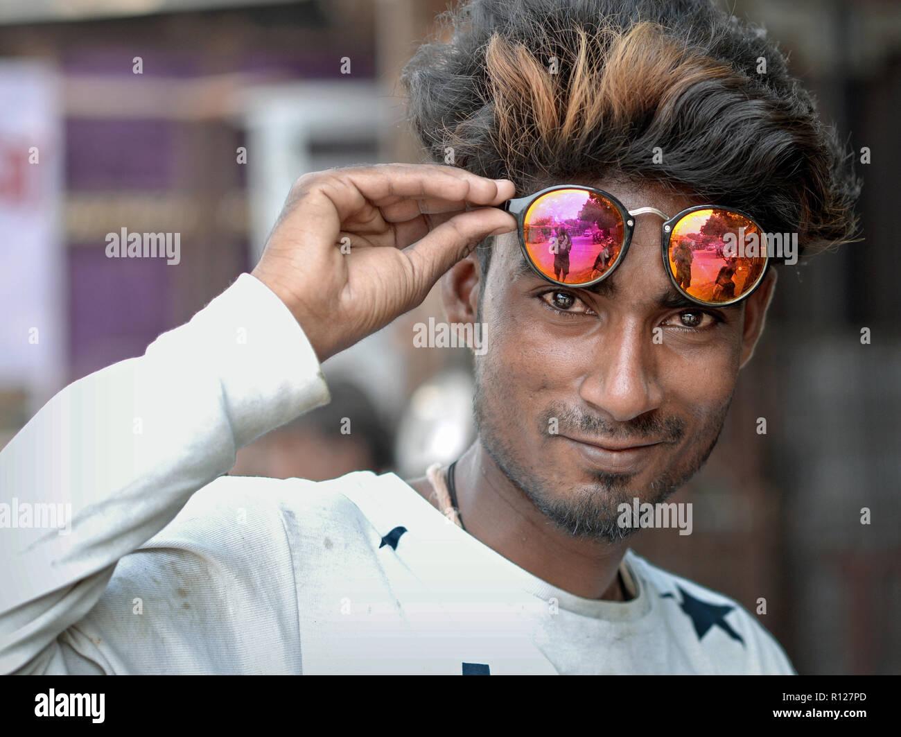Bello, giovane uomo di Rajasthani detiene il mirroring di occhiali da sole con la sua mano destra sulla sua fronte e guarda nella telecamera. Foto Stock
