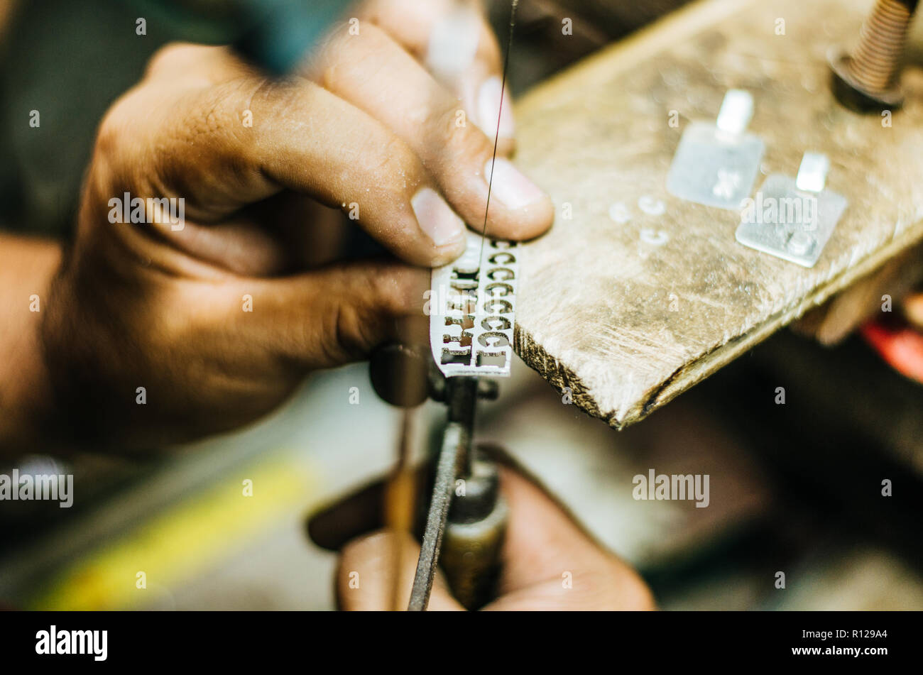 Uomo con le mani in mano di oreficeria su un pezzo di argento con una sega per metalli sul tavolo da lavoro, close up, selezionata la messa a fuoco e profondità di campo ridotta Foto Stock