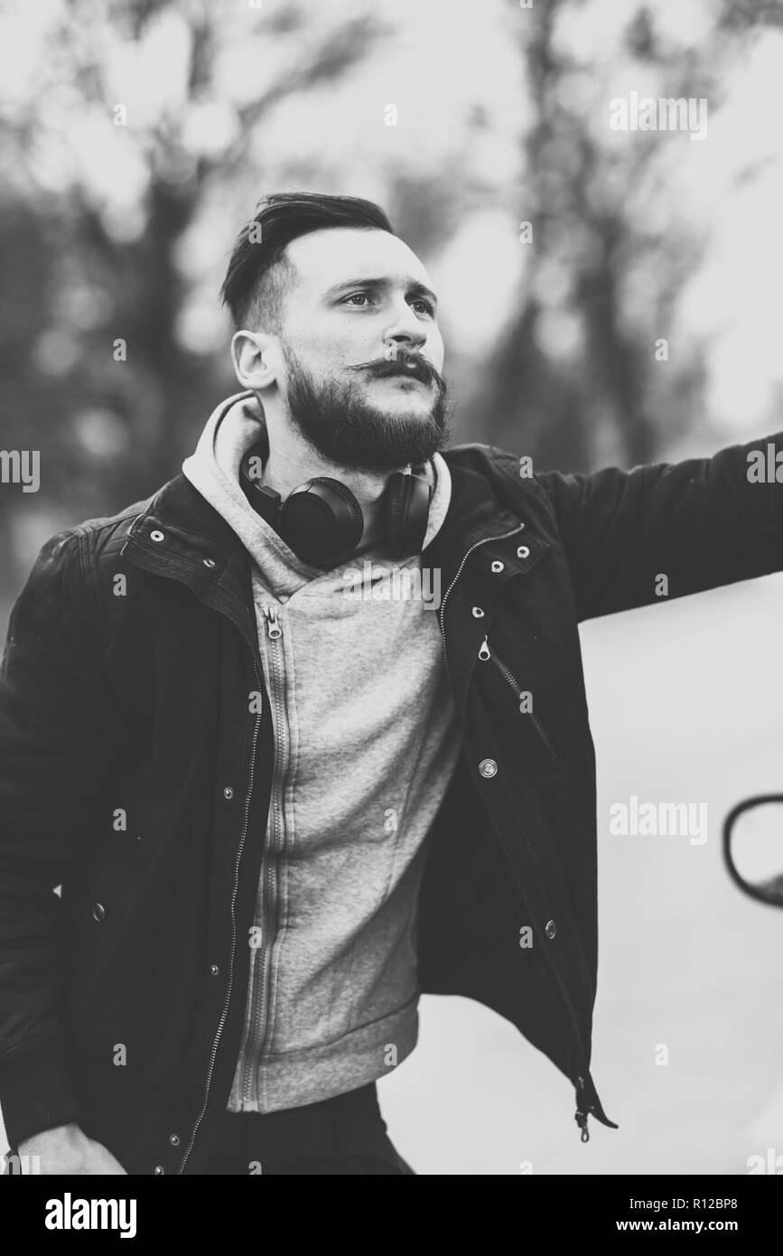 Un bel giovane hipster uomo in piedi accanto alla sua auto e in attesa. Foto Stock
