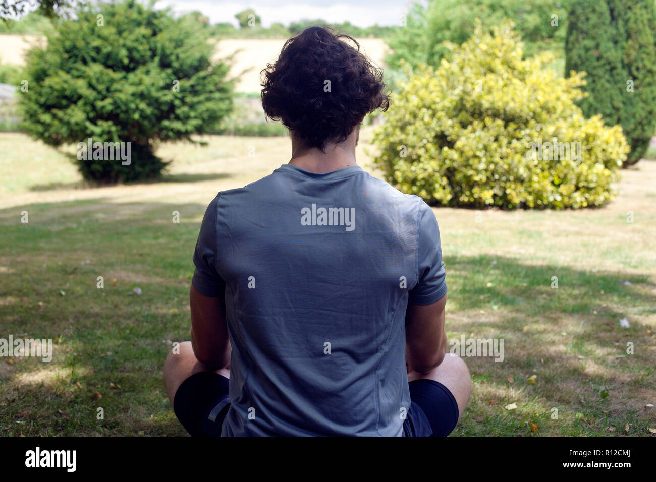 Giovane uomo a praticare yoga in giardino, vista posteriore lotus pongono Foto Stock