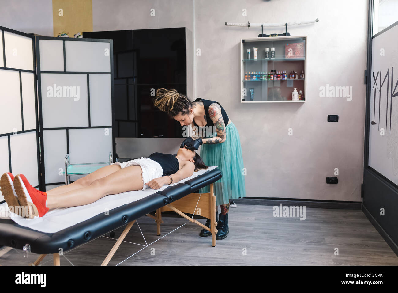 Tattooist frequentando il cliente nel salottino Foto Stock