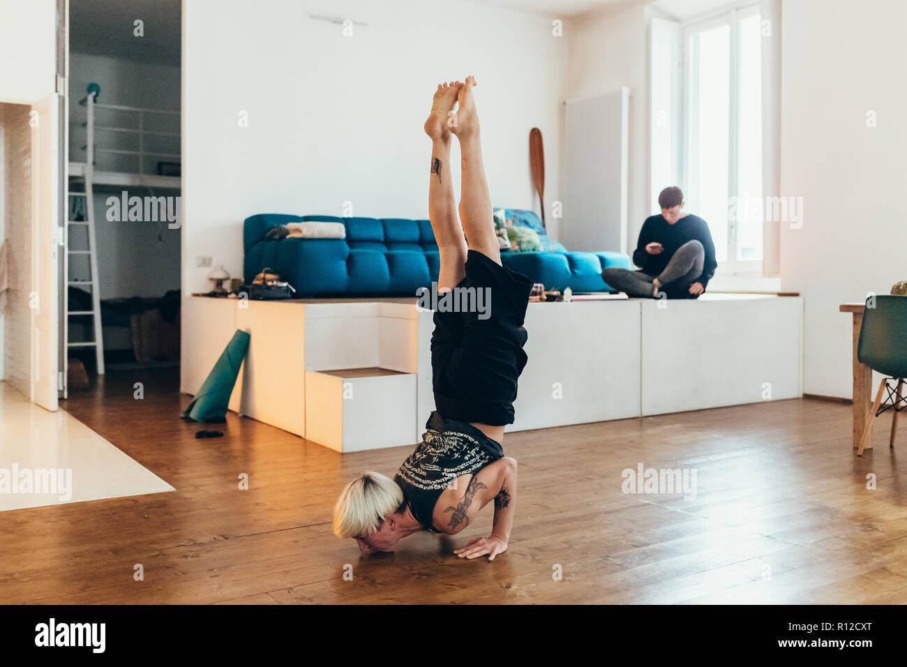 La donna a praticare yoga a casa, un amico in background Foto Stock