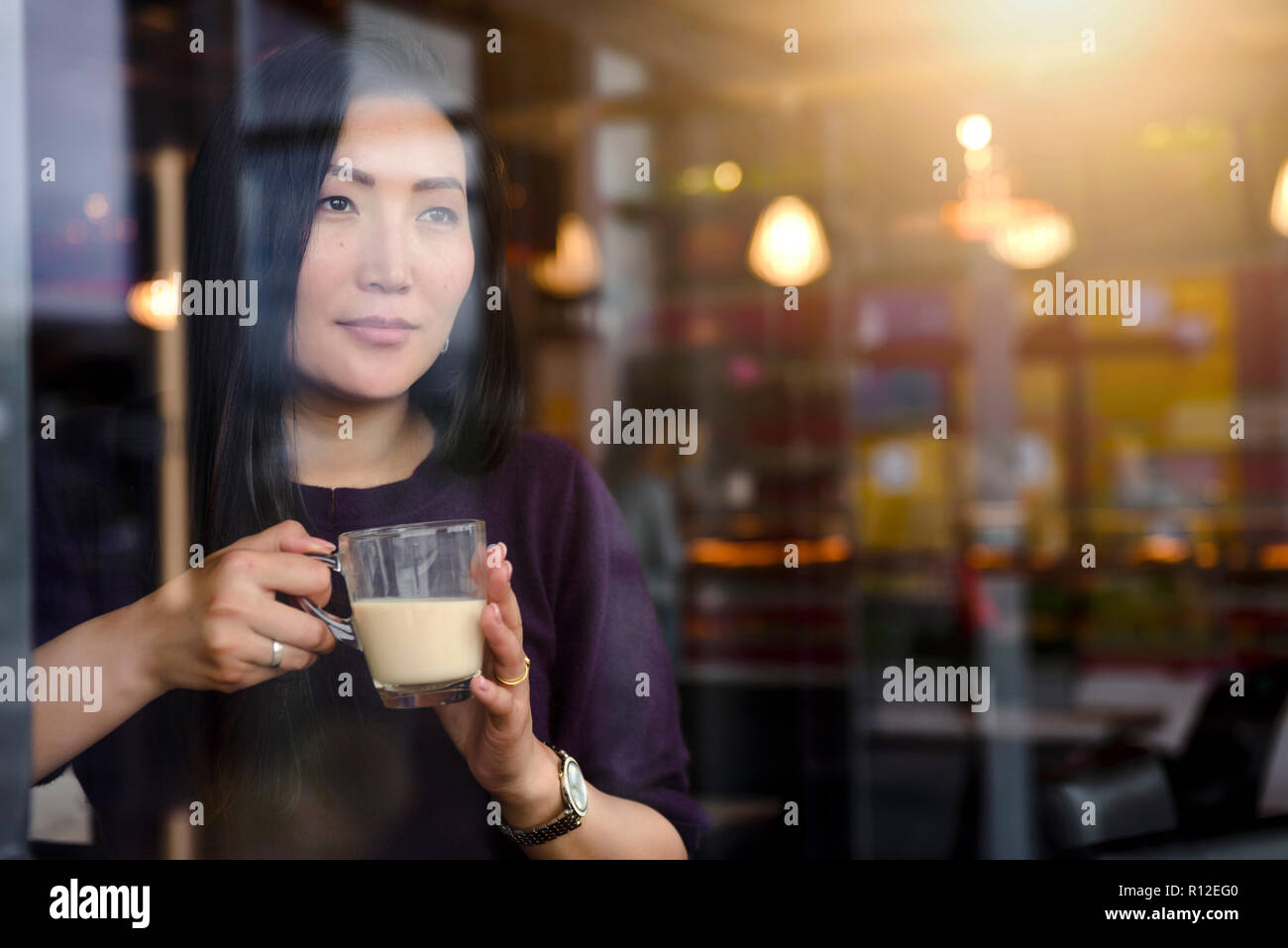 Metà donna adulta con caffè guardando fuori dalla finestra cafe sede Foto Stock