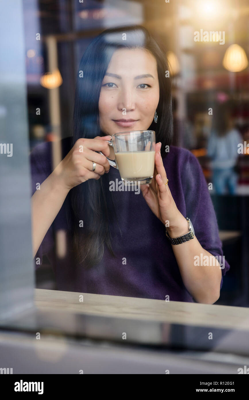 Metà donna adulta con caffè guardando fuori dalla finestra cafe sedile, ritratto Foto Stock