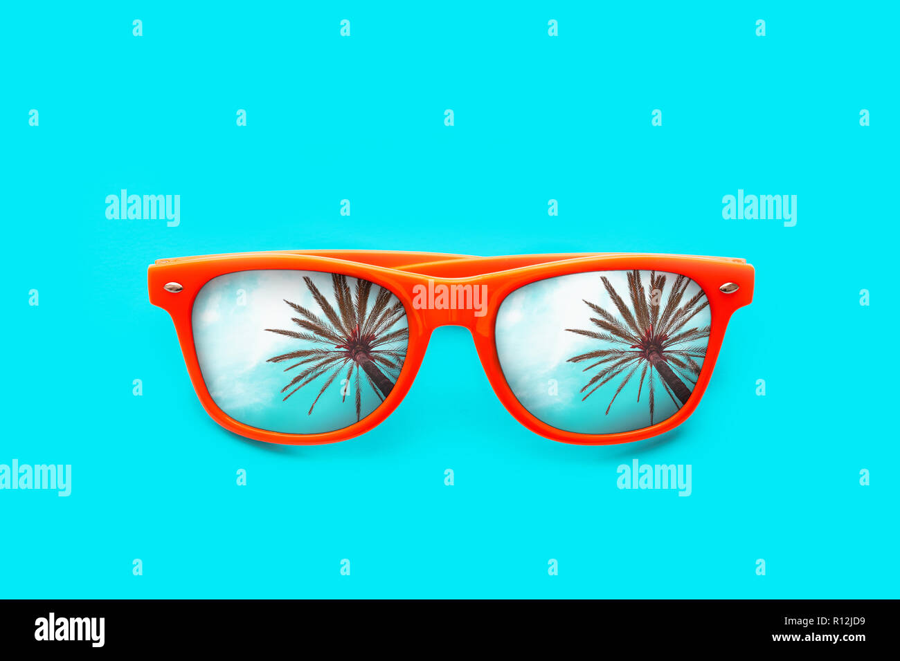 Occhiali da sole arancione con Palm tree riflessioni isolato in un intenso blu ciano sfondo. La minima nozione di immagine per pronto per l'estate, protezione solare, acqua calda Foto Stock